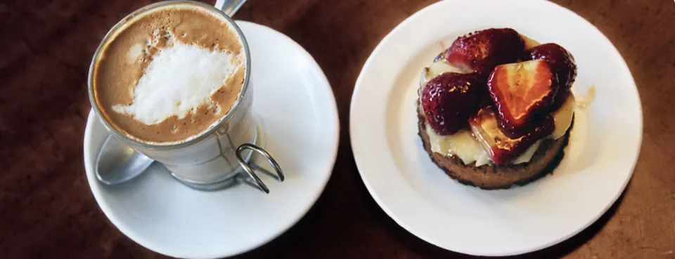 Un cortado y una tartaleta de fresa servidos sobre la barra.