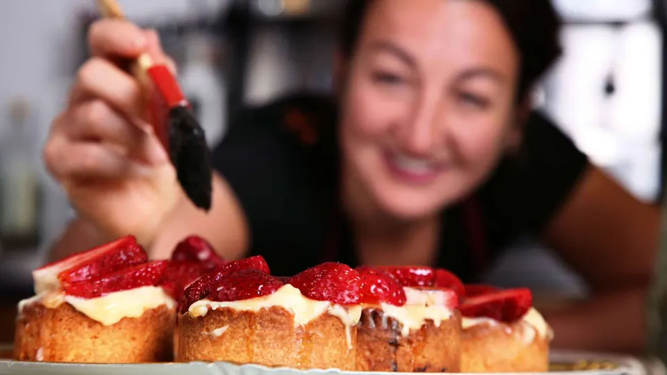 En el obrador, una pastelera coloca fresas sobre las tartaletas con una manga.