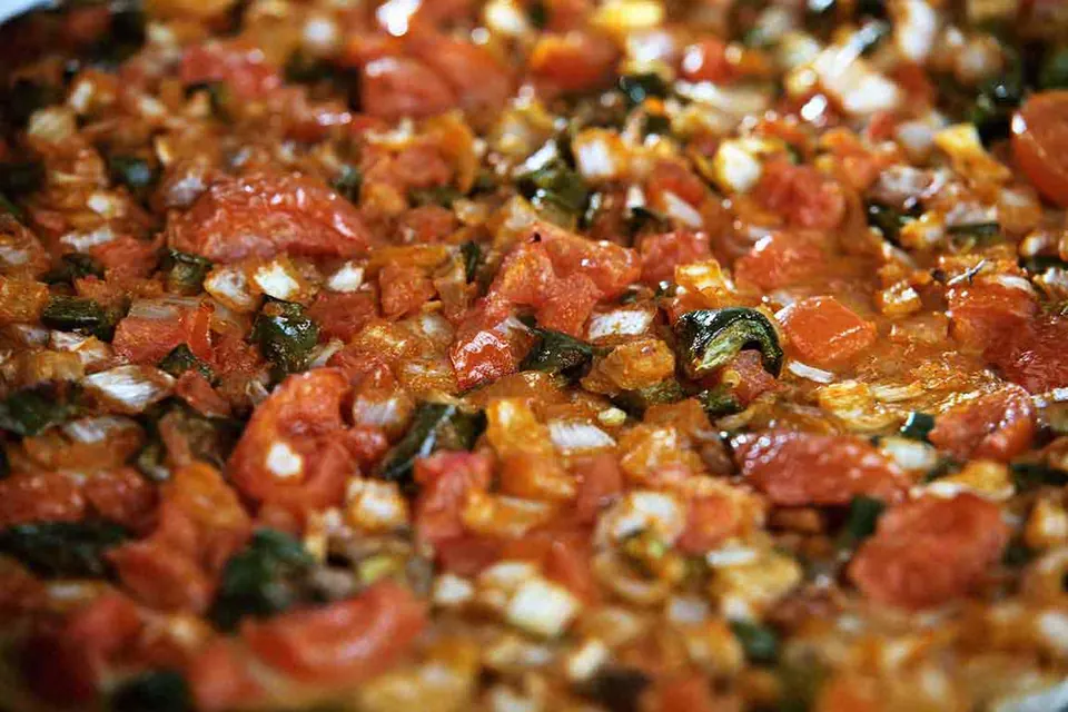 Coca de verdura recién hecha, cubierta de tomate, pimiento y cebolla.