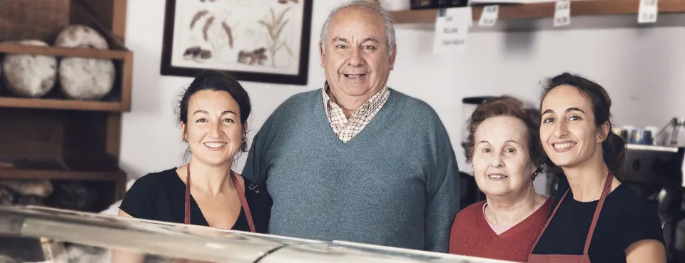 Cuatro personas de la familia sonríen detrás del mostrador de la pastelería, con las estanterías de pan al fondo.