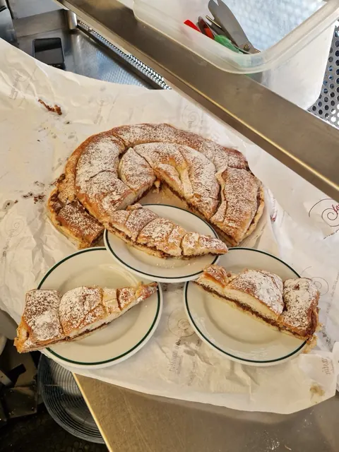 Ensaimada de chocolate espolvoreada con azúcar glas, cortada en porciones sobre platos.