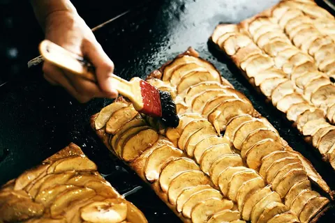 Bandejas de hojaldre de manzana con las láminas colocadas en fila, pinceladas con brillo.